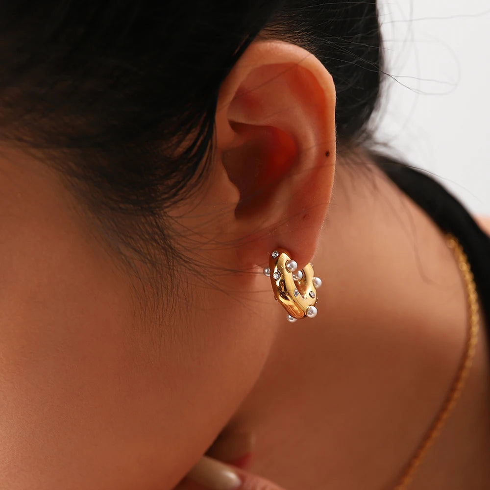A close-up image of a woman's ear wearing an 18K gold plated hoop earring with zircon and pearl accents.