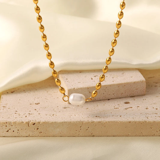 A gold-plated bead chain necklace with a single pearl pendant resting on a beige stone surface.