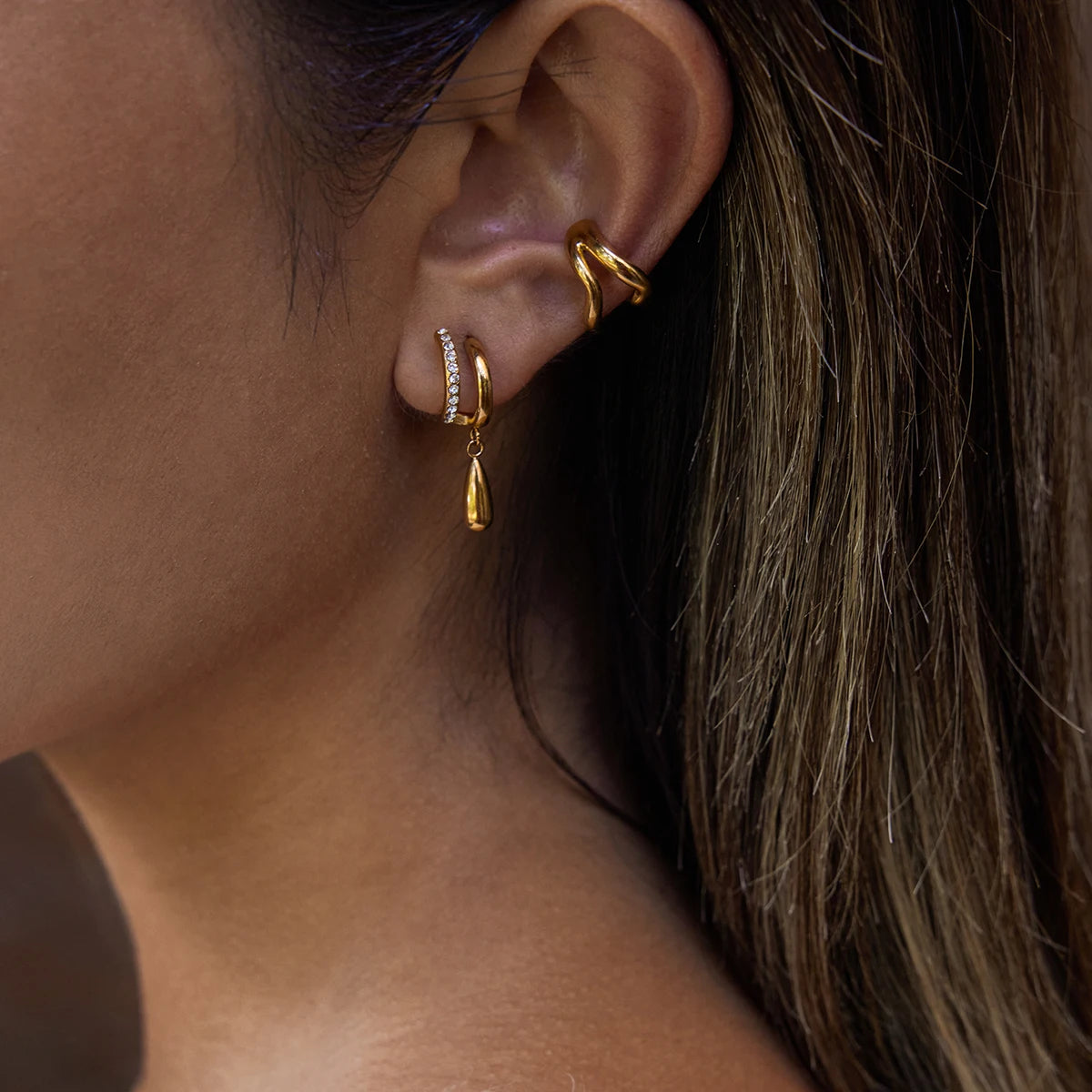 Close-up of an ear wearing gold hoop earrings with a blurred background