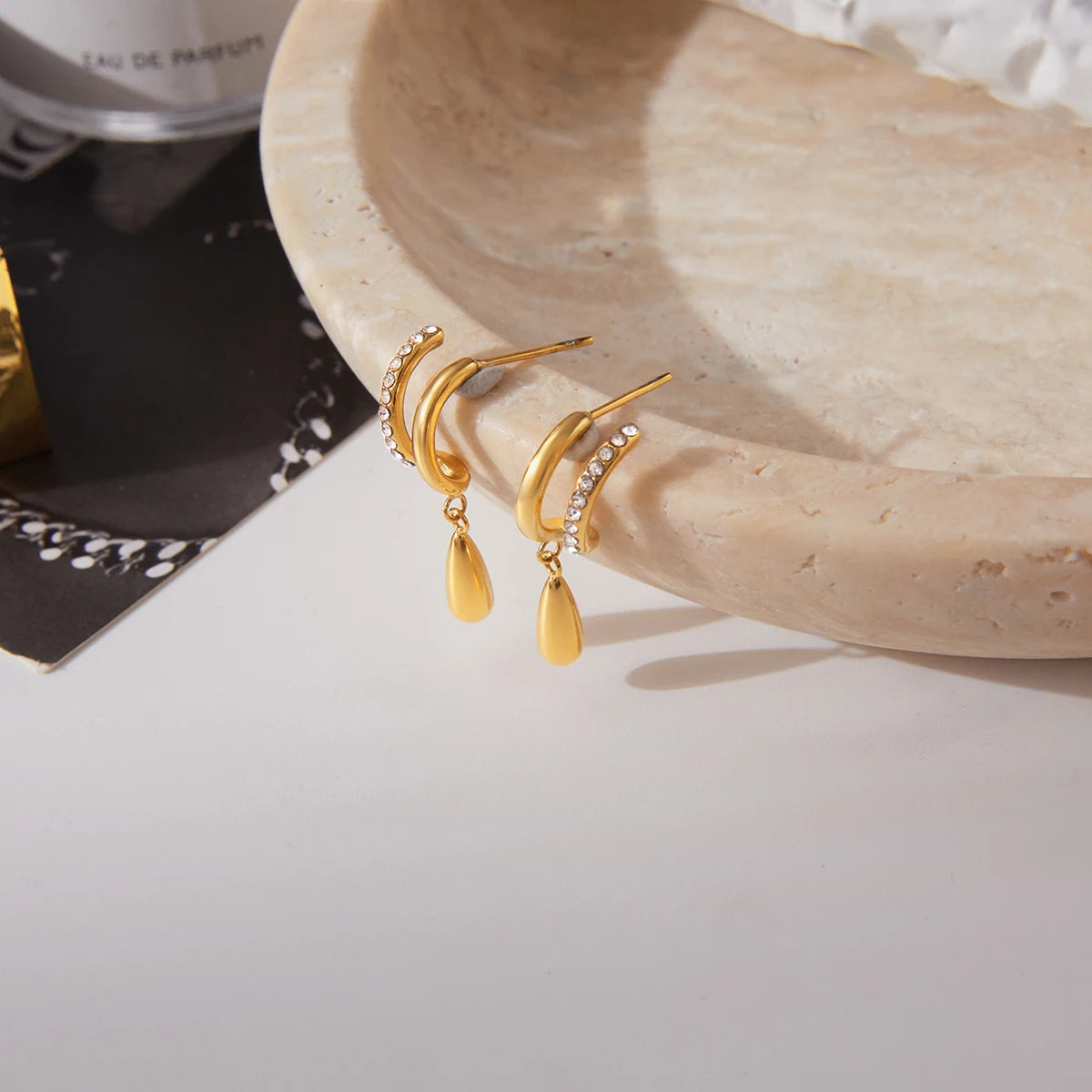 Gold earrings with a decorative design on a beige stone surface.