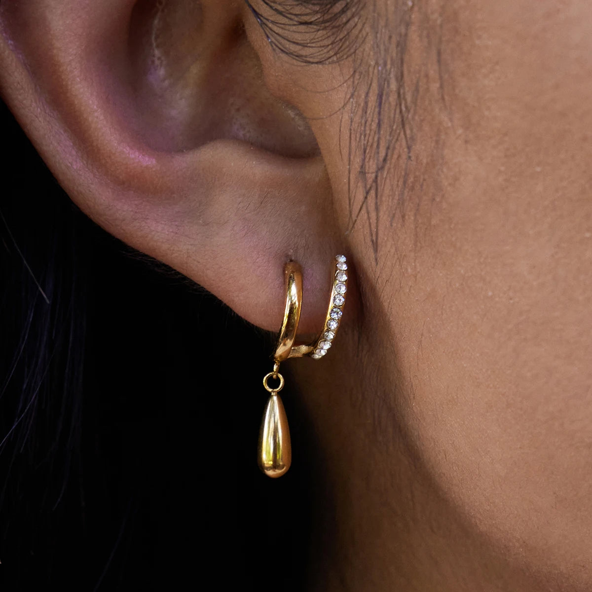 Close-up of an ear wearing gold hoop earrings with a teardrop pendant.