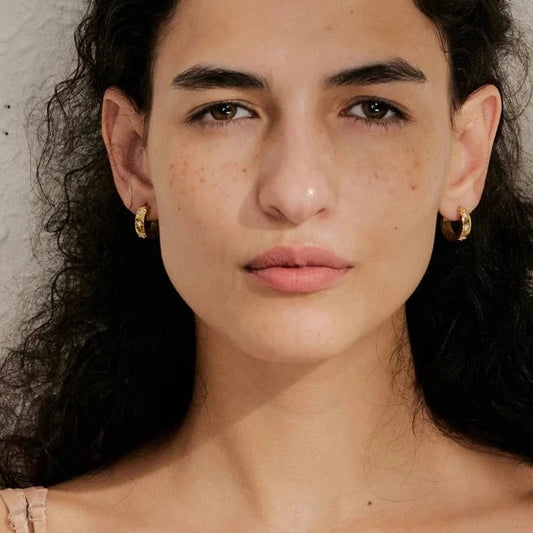 Close-up of a person with dark hair and earrings against a neutral background