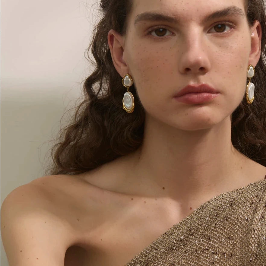 Woman wearing gold earrings with a neutral background