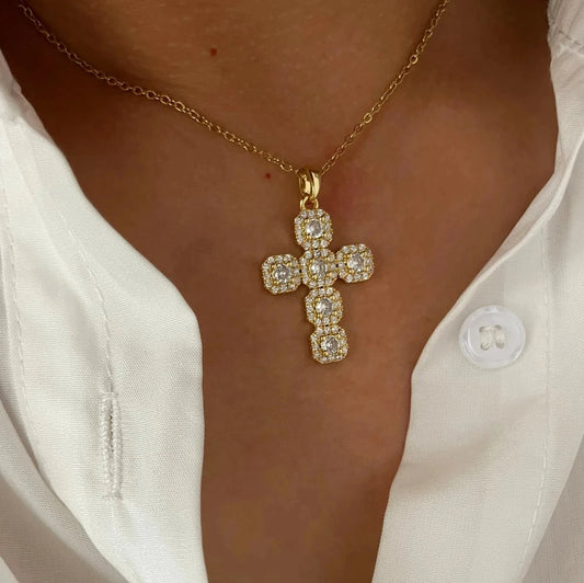 Gold cross necklace with clear stones on a person wearing a white shirt.