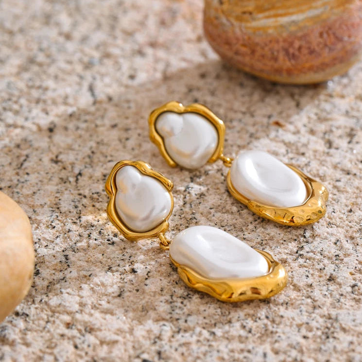 Gold earrings with white stones on a textured surface