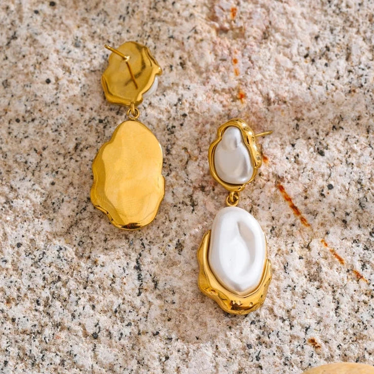 Gold and pearl earrings on a textured surface