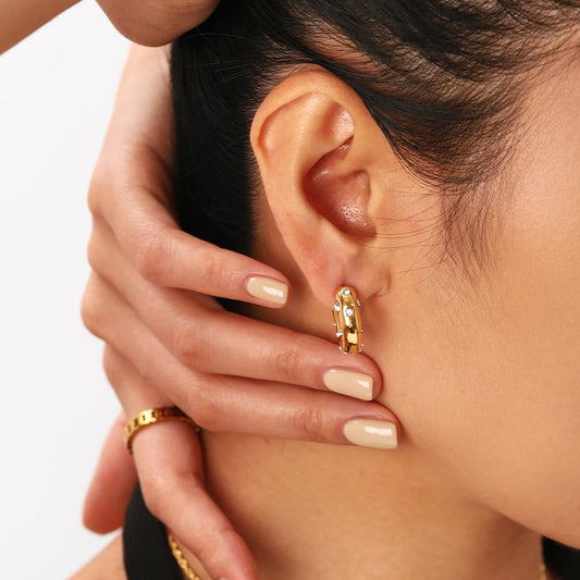 A close-up image of a woman's ear wearing a gold-plated hoop earring with a sparkling zirconia stone.